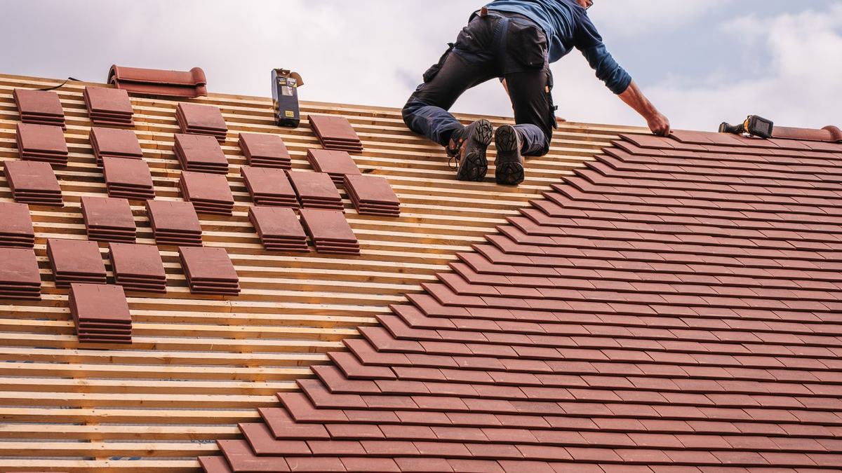 Dachdecker deckt ein Steildach mit roten Tonziegeln neu ein