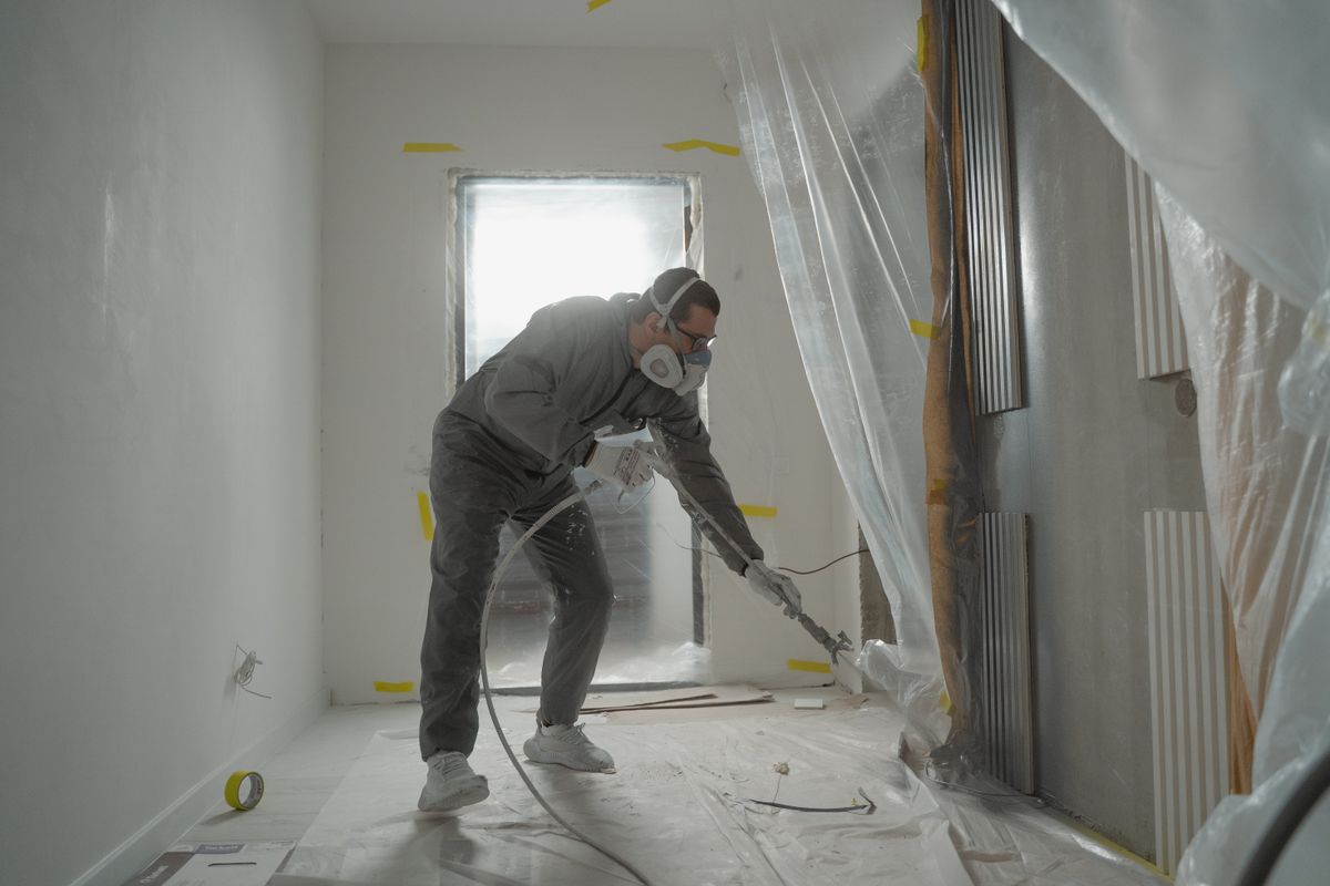 Maler spritzt eine abgeklebte Wand mit dem Airless-Gerät